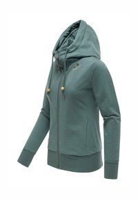 Sweat à capuche vert avec fermeture éclair, col montant, capuche ajustable à cordon avec perles en bois, et manches longues avec poignets côtelés.