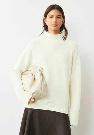 Weißer gestrickter Pullover mit hohem Rippkragen und überschnittenen Schultern; kombiniert mit einer weichen beigen Zugbandtasche und einem dunklen Rock.