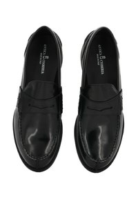 Scarpe in pelle nera con finitura lucida, dotate di un design slip-on, cuciture decorative e un piccolo dettaglio vicino alla tomaia.