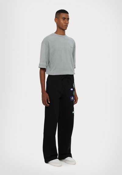 Lys grå bomulls t-skjorte med rullede ermer, kombinert med svarte sweatpants med forskjellige fargerike lapper, og hvite sneakers.
