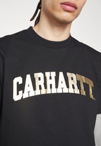 Černé bavlněné tričko s velkým zlatým fóliovým logem "CARHARTT" v tučném písmu na hrudi. Klasický design s kulatým výstřihem.