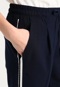 Granatowe dresy z elastycznym pasem, bocznymi kieszeniami i białym paskiem bocznym dla kontrastu. Materiał wydaje się gładki i lekki.