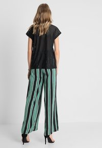 Mustat paita, jossa on pystysuoria poimuja, yhdistettynä leveisiin housuihin, joissa on mustia ja mintunvihreitä pystysuoria raitoja. Mustat korot näkyvät.