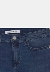 Granatowe dżinsy z klasycznym stanem, zapięcie na srebrny guzik oraz metką Calvin Klein Jeans na górze. Subtelna tekstura i szwy.