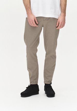 Beige Hosen mit strukturiertem Finish, schlankem Schnitt und umgenähten Säumen, kombiniert mit schwarzen Wildlederschuhen. Einfaches weißes T-Shirt getragen.