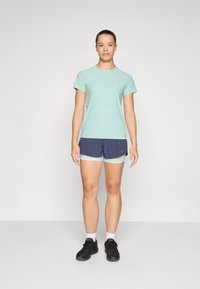 Lyseblå treningst-skjorte kombinert med marineblå shorts med mintgrønn detalj. Iført svarte sneakers og hvite sokker.