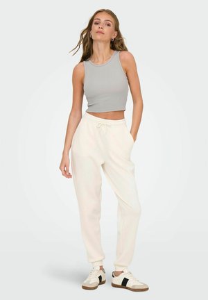 Graues, kurzes Tanktop mit gerippter Textur, kombiniert mit cremefarbenen Jogginghosen mit elastischem Bund und gerippten Säumen, ergänzt durch Sneakers.