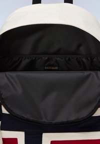 L'interno dello zaino presenta un rivestimento in tessuto nero, un coperchio superiore bianco e un'etichetta del marchio visibile. L'apertura con zip rivela un compartimento spazioso.