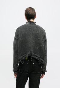 Sweater cortado em malha cinza escuro com bainhas desfiadas, decote franzido e acabamentos metálicos circulares. Apresenta um design texturizado e um ajuste solto.