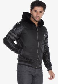Black bomber jacket with textured snake-skin sleeves, zip front, hood, and horizontal stripes. Features a smooth body and soft inner lining.