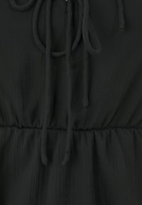 Svart plagg med en strukturerad tyg, som har en dragsko vid halslinningen och en samlad midja, vilket skapar en flödande silhuett.