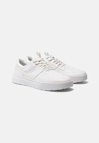 Sneakers atletici bianchi con tomaia in pelle texturizzata, dettagli perforati e suola in gomma con scanalature per una migliore aderenza.