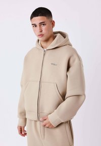 Felpa con cappuccio beige con zip, ampia tasca frontale, tessuto morbido e cappuccio, con un piccolo logo nella parte superiore sinistra.