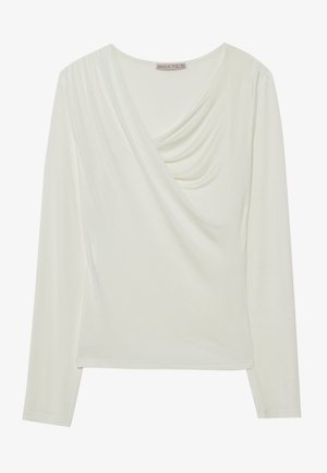 Top de manga larga en color crema con un diseño de escote en V drapeado, textura suave y silueta ajustada con un dobladillo redondeado. Etiqueta de la marca visible.