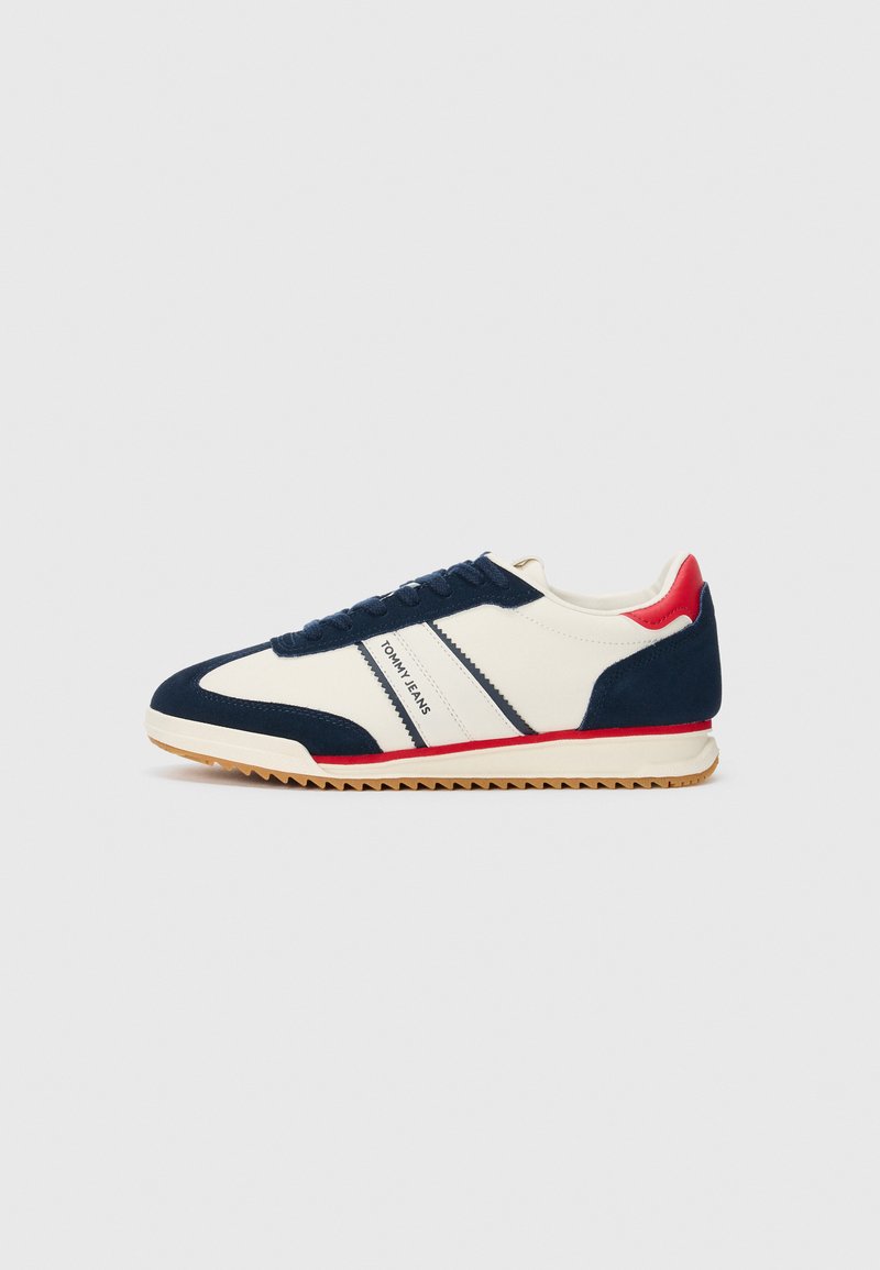Baskets blanches avec des accents bleu marine et rouge, semelle texturée, design à lacets, et marquage "Tommy Jeans" sur le côté.