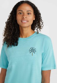 Camiseta de algodón azul claro con un diseño de palmera bordado en negro y dorado en el pecho. Corte relajado con mangas cortas.