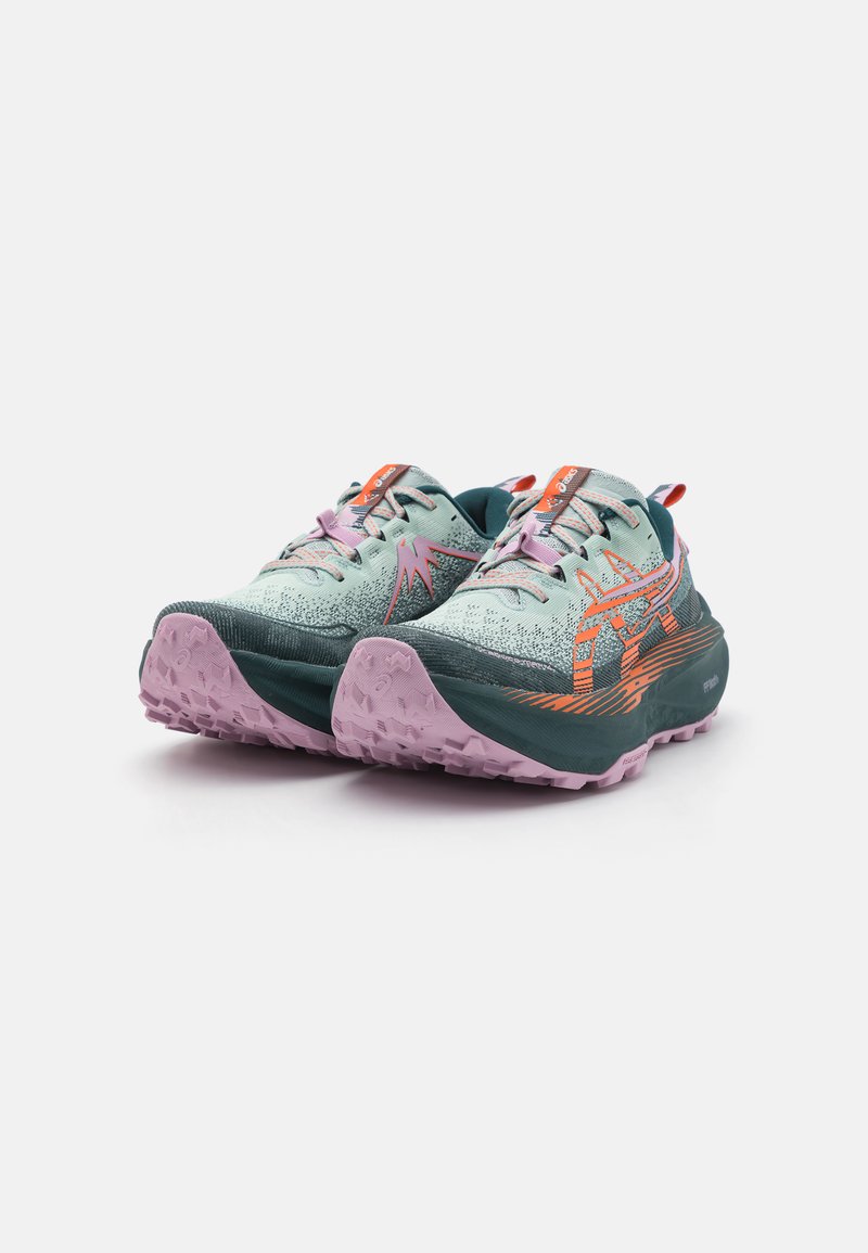 Zapatillas de trail running con un upper verde menta con acentos naranjas, un patrón texturizado y una suela rosa y resistente para tracción.
