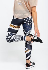 Legginsy sportowe o wysokim stanie z mieszanką wzorów geometrycznych i zwierzęcych w kolorach granatowym, białym i złotym, wykonane z gładkiego, elastycznego materiału.