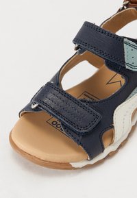 Navy blue sandal with a textured leather upper, adjustable velcro straps, beige insole, and a light brown rubber sole.