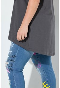 T-shirt gris à coupe décontractée, associé à un jean bleu déchiqueté avec des accents de crâne rose et d'écriture à la main.