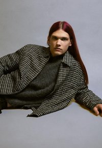 Czarnobiała kurtka w kratę z teksturowanym wykończeniem, noszona na ciemnoszarym, puszystym swetrze, z zapięciem na zamek i otwartym kołnierzem.