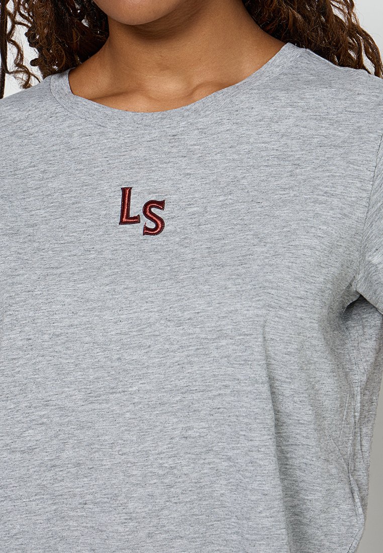 Graues Baumwoll-T-Shirt mit rundem Halsausschnitt, mit roten gestickten Buchstaben "LS" auf der linken Seite. Weicher, strukturierten Stoff, kurze Ärmel.