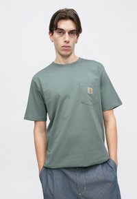 Πράσινο βαμβακερό μπλουζάκι με στρογγυλή λαιμόκοψη και κοντά μανίκια. Διαθέτει τσέπη στο αριστερό στήθος και τετράγωνη ετικέτα με λογότυπο. Ομαλή υφή.