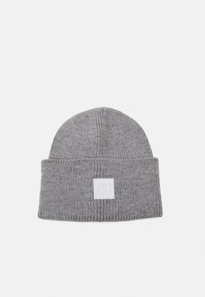 Grå strikket hue med en foldet kant og et kvadratisk logo-patch. Stoffet er ribbet, hvilket giver struktur og elasticitet.