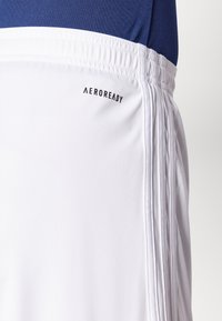 Shorts de sport blancs avec la marque Aeroready, dotés d'une ceinture texturée et de rayures verticales sur les côtés.