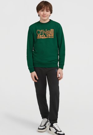 Grön sweatshirt med orange text "O'Neill Santa Cruz", ihop med svarta joggingbyxor och vita sneakers, står på en enkel bakgrund.