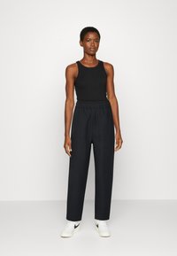 Top de tanque sem mangas preto, combinado com calças largas de cintura alta pretas com uma faixa elástica na cintura e bolsos laterais; usado com tênis brancos.