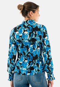 Blusa a maniche lunghe con motivo floreale in tonalità di blu e nero. Presenta un colletto con bottoni e polsini arricciati. Tessuto leggero.