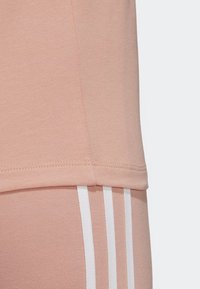 Ljus rosa träningsöverdel, mjuk bomullsblandning, med rak passform och liten fåll. Vertikala vita ränder på matchande underdel.