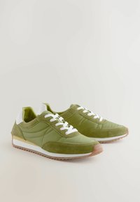 Grønne sneakers lavet af en kombination af glatte og ruskinds materialer, hvide snørebånd, gummisål og et lavprofil design.
