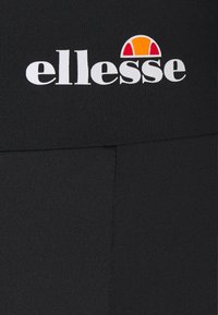 Tissu noir avec logo ellesse blanc et un motif en demi-cercle orange et rouge au-dessus du texte, probablement sur un vêtement.