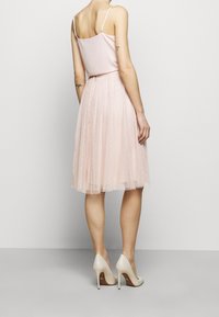Robe rose clair avec un haut en satin et une jupe en tulle, présentant un design plissé et de petits détails en pois. Assortie à des talons hauts beiges.