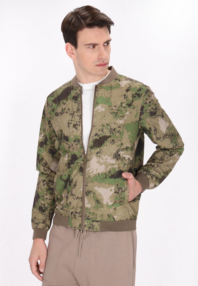 Giacca bomber mimetica nelle tonalità di verde e marrone, con zip frontale, polsini a costine e tasche laterali con chiusura a scatto.