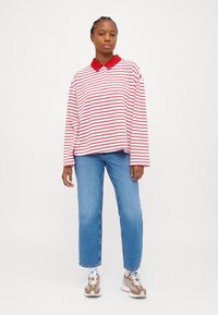 Tricou polo cu mânecă lungă, cu dungi roșii și albe, guler roșu, asortat cu blugi drepti de culoare bleu deschis și adidași bej.