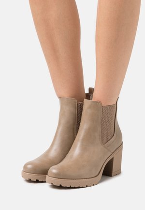Botines beige con un acabado de cuero liso y paneles laterales elásticos texturizados. Cuentan con un tacón grueso y una suela de goma resistente.