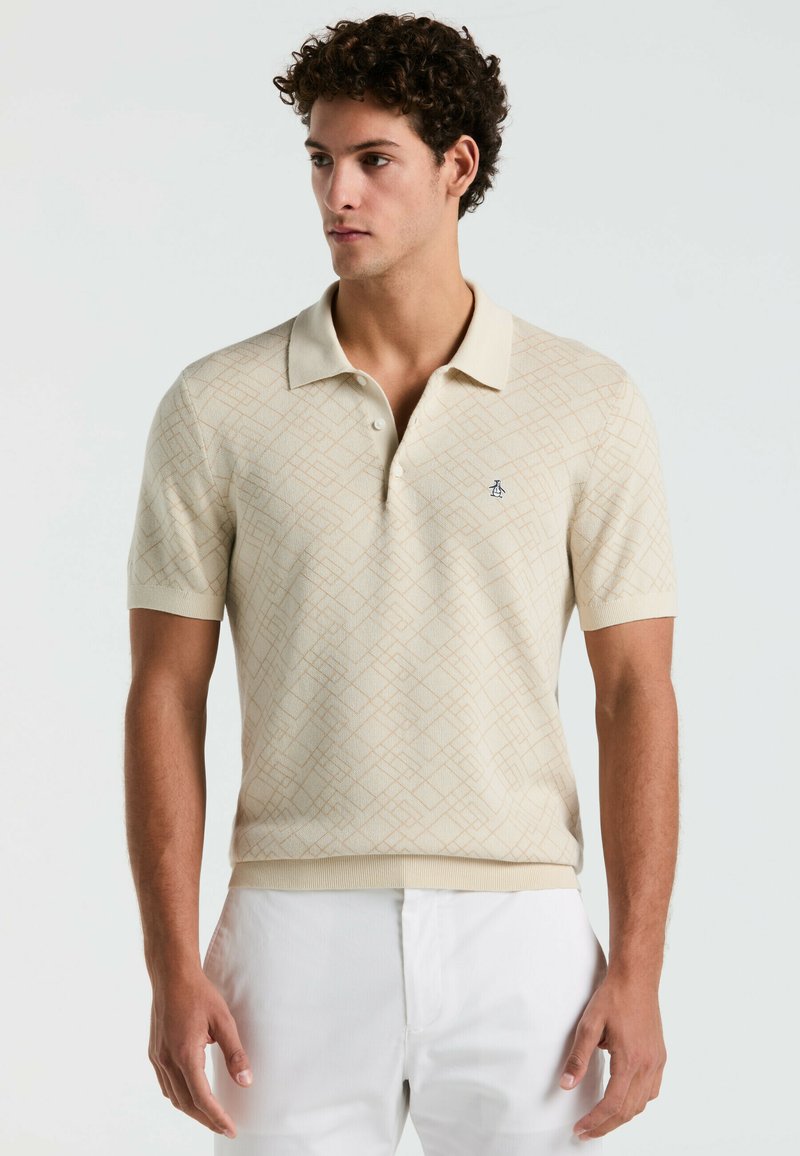 Polo beige en tissu tricoté, arborant un motif géométrique dans des tons de brun clair, manches courtes et col avec un logo.