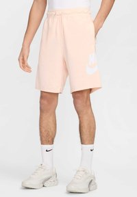 Bermudas de algodão cor-de-rosa claro com um logotipo Nike branco, cintura elástica com cordão e bolsos laterais; usadas com meias brancas e ténis.