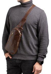Borsa a tracolla in pelle marrone con due tasche con zip, tracolla regolabile, superficie liscia e forma arrotondata, indossata attraverso il torso.