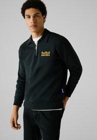 Zwarte, met rits broek met geribbelde manchetten en zoom. Voorzien van het gele "Red Bull Racing" logo op de borst. Gemaakt van een zachte stoffenmix.