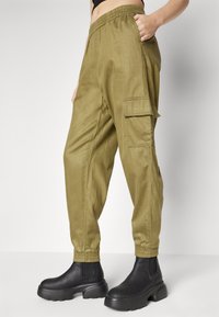 Olivgröna cargobyxor i mjukt material, med elastisk midja, sidofickor och en cargoficka vid låret. Svarta ankelboots fulländar looken.