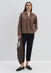 Bruine lange mouwen shirt met een kraag en een trekkoordhalslijn, gecombineerd met zwarte tapered pants, zwarte instap schoenen en een mesh tote bag.