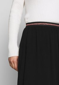 Gonna nera con un design testurizzato e fluido, caratterizzata da un sottile accento rosso lucido in vita, indossata con un maglione fitted bianco a coste.