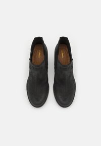 Sorte slip-on sko i ruskind med runde snuder, elastiske sidespaneler, mandelformet design og brune lædersåler.