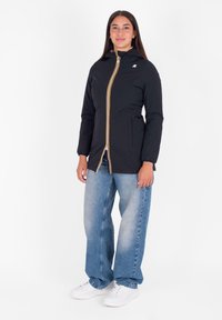 Giacca nera con cappuccio, zip gialla e bianca, due tasche laterali e polsini elastici. Abbinata a jeans larghi blu chiaro e sneaker bianche.