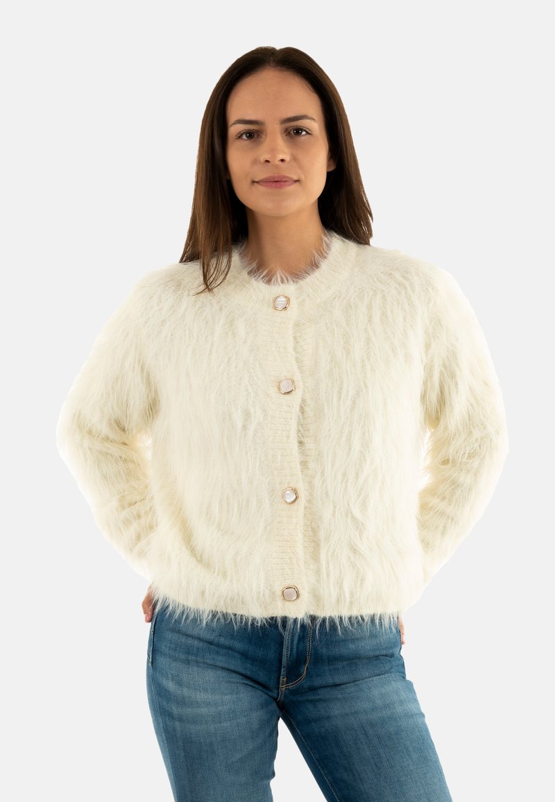 Cardigan bianco e soffice con una finitura texturizzata, caratterizzato da bottoni rotondi e un colletto a coste, abbinato a jeans in denim blu.