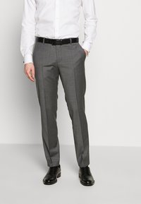 Grau gestaltete Stoffhose mit einer subtilen Textur, gerade geschnitten und mit Seitentaschen, getragen mit einem weißen Hemd und schwarzen Schuhen.